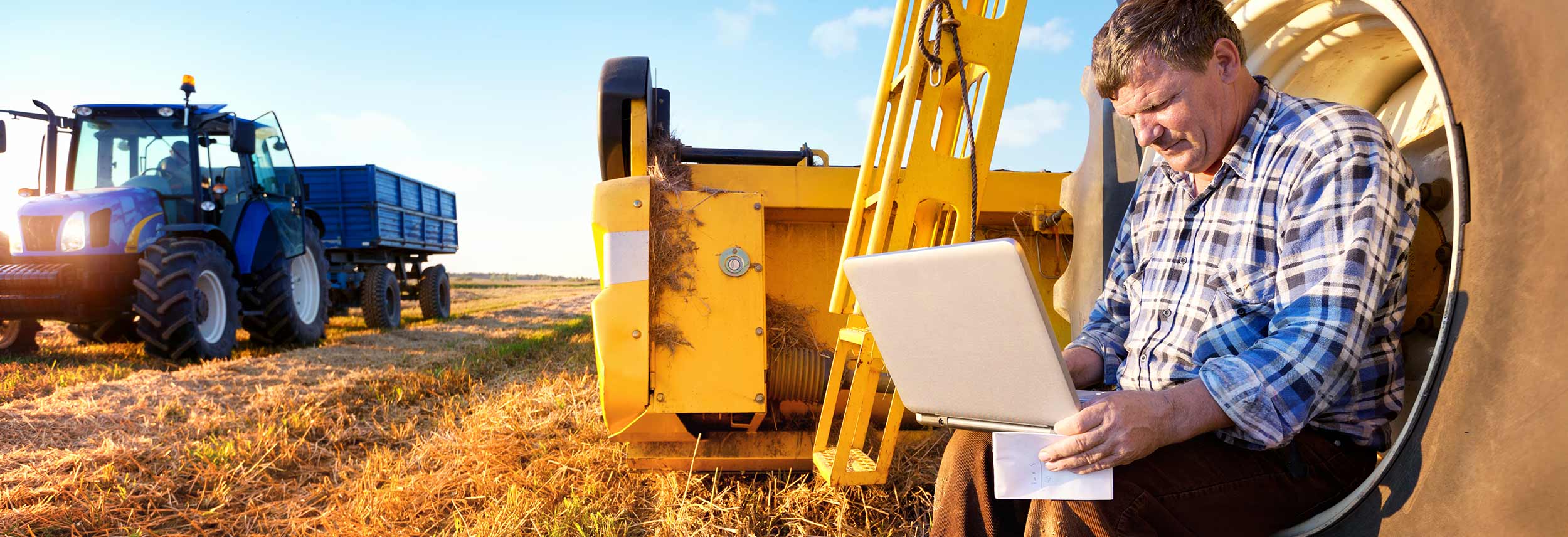 Farmer with Laptop in the field with harvesting equipment